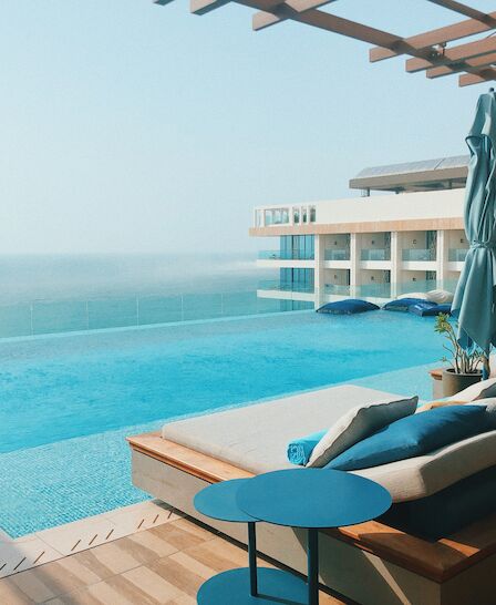 A luxurious terrace with a pool, sunbeds, umbrellas, and a stunning sea view, perfect for a relaxing day by the water.