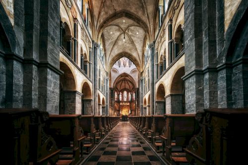 The image shows the interior of a grand church or cathedral with high arched ceilings, stone columns, and rows of pews leading to the altar.