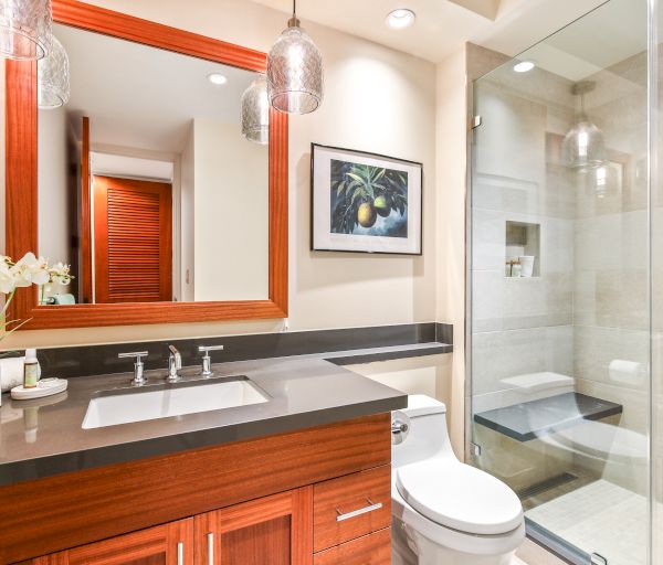 A modern bathroom with a wooden vanity, a mirror, a sink, a toilet, a shower with a glass door, and decorative elements including a plant and artwork.
