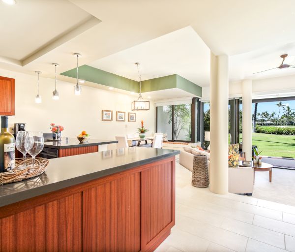 A modern open-plan kitchen and living area with wooden cabinetry, pendant lights, and large glass doors opening to a patio and garden area.