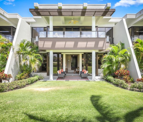 A modern, two-story building with large windows, balconies, and a well-manicured lawn surrounded by tropical plants and palm trees ends the sentence.