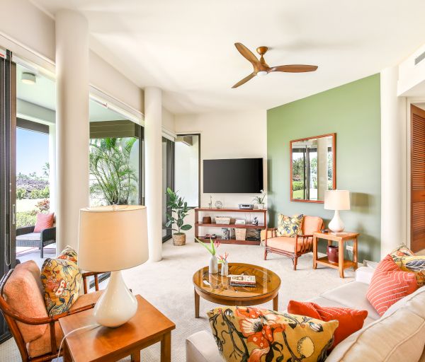 A bright living room with a green accent wall, modern furniture, TV, ceiling fan, large windows, and a door leading to a patio with garden views.