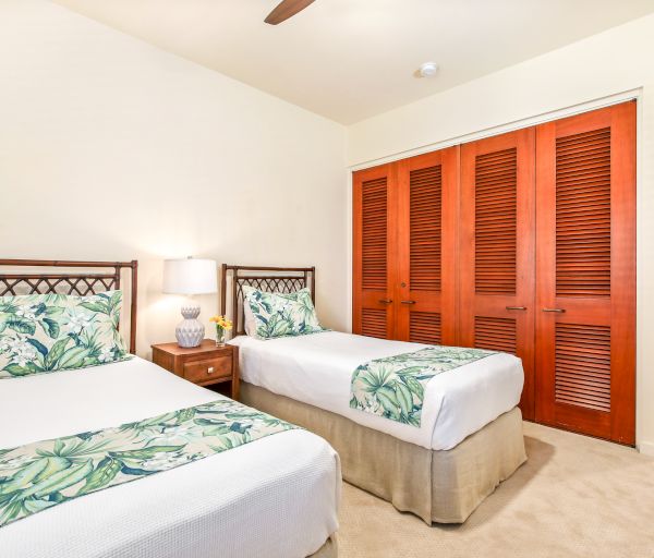 A tidy bedroom with two twin beds, tropical-themed bedding, a nightstand with a lamp, and a large wooden closet.