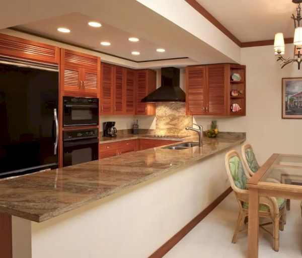 A modern kitchen with wooden cabinetry, an island with granite countertops, a dining area with a glass table and chairs.