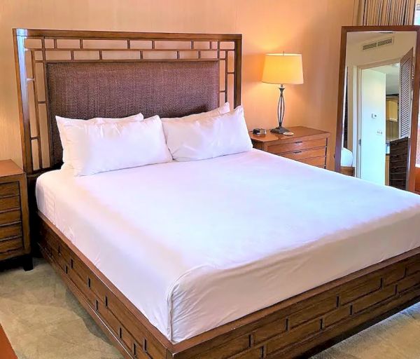 A neatly arranged bedroom features a large bed with white linens, wooden headboard, nightstands with lamps, and a tall mirror.