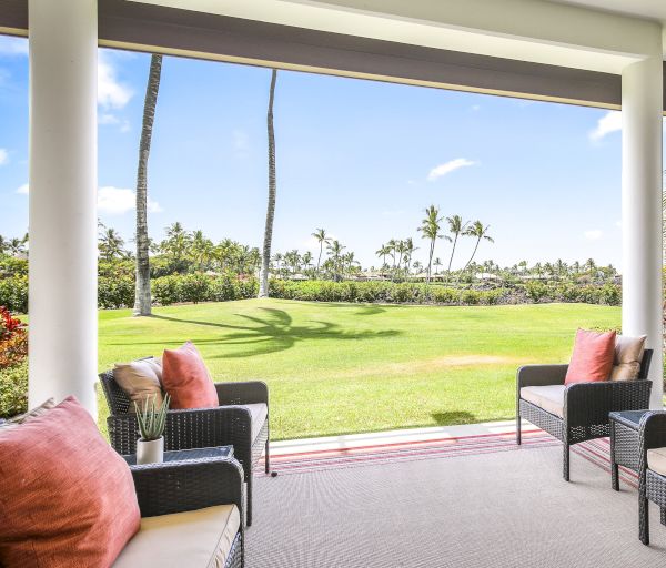 The image shows an outdoor patio with wicker furniture and pink cushions, overlooking a grassy area with palm trees in the background.