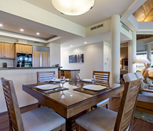 This image displays a modern dining and living area with wooden furniture, set dining table, open kitchen, cozy seating, and large windows.
