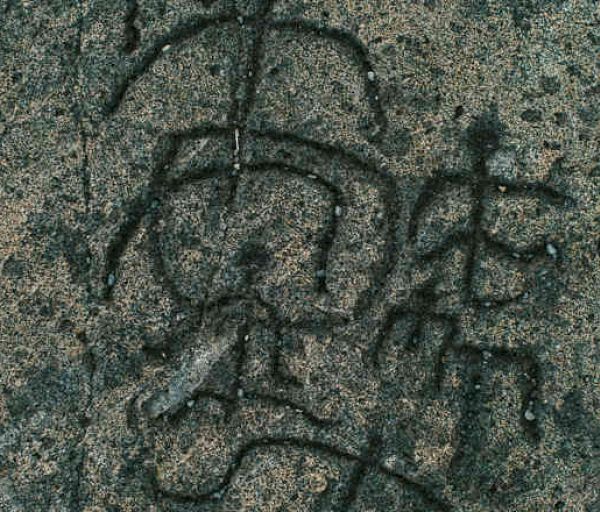 This image shows carvings or engravings of ancient or traditional symbols or characters on a rough stone surface.