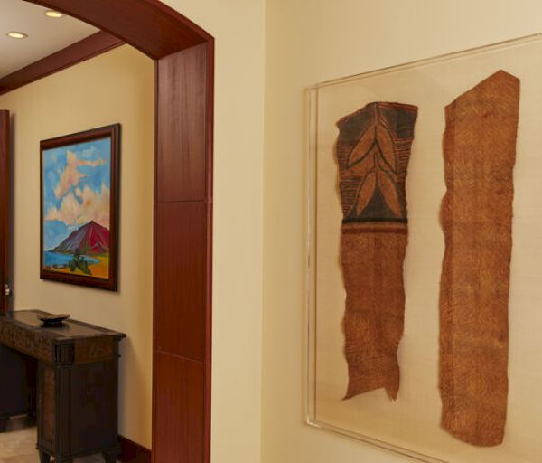 The image shows a hallway with framed traditional art pieces on the wall and a small console table with decorative items. There's a colorful painting.