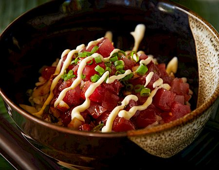 A bowl of diced raw fish, likely tuna, topped with green onions and drizzled with a sauce, possibly mayonnaise, arranged in a brown bowl.