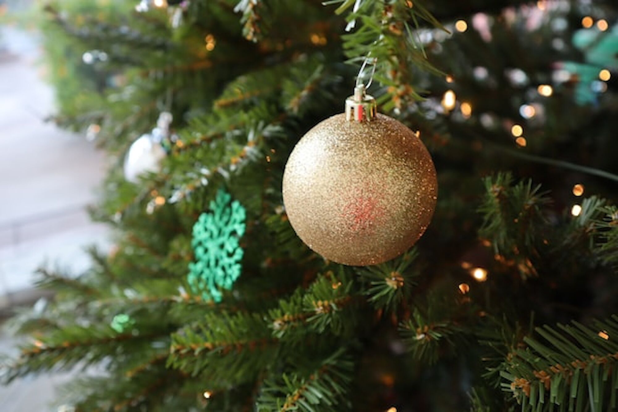The image shows a sparkling gold Christmas ornament hanging on a decorated evergreen tree, enhancing festive cheer.