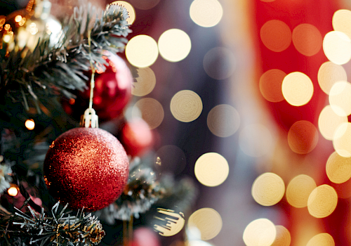A festive Christmas tree with red baubles and blurred colorful lights in the background, creating a warm holiday glow.
