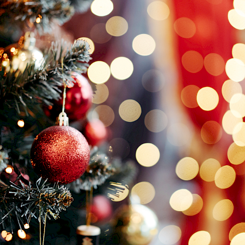 A festive Christmas tree with red baubles and blurred colorful lights in the background, creating a warm holiday glow.