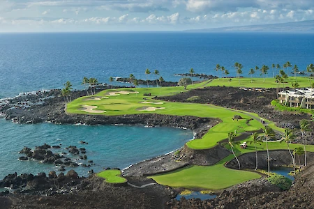 A rocky coastal golf course perched by the sea, with green fairways, palm trees, and blue ocean views along lava rocks, in a sunny tropical setting.