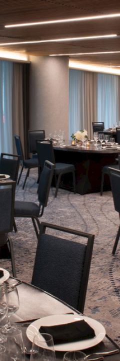 The image shows an elegantly set banquet hall with round tables, black chairs, plate settings, glassware, napkins, and decorative centerpieces.
