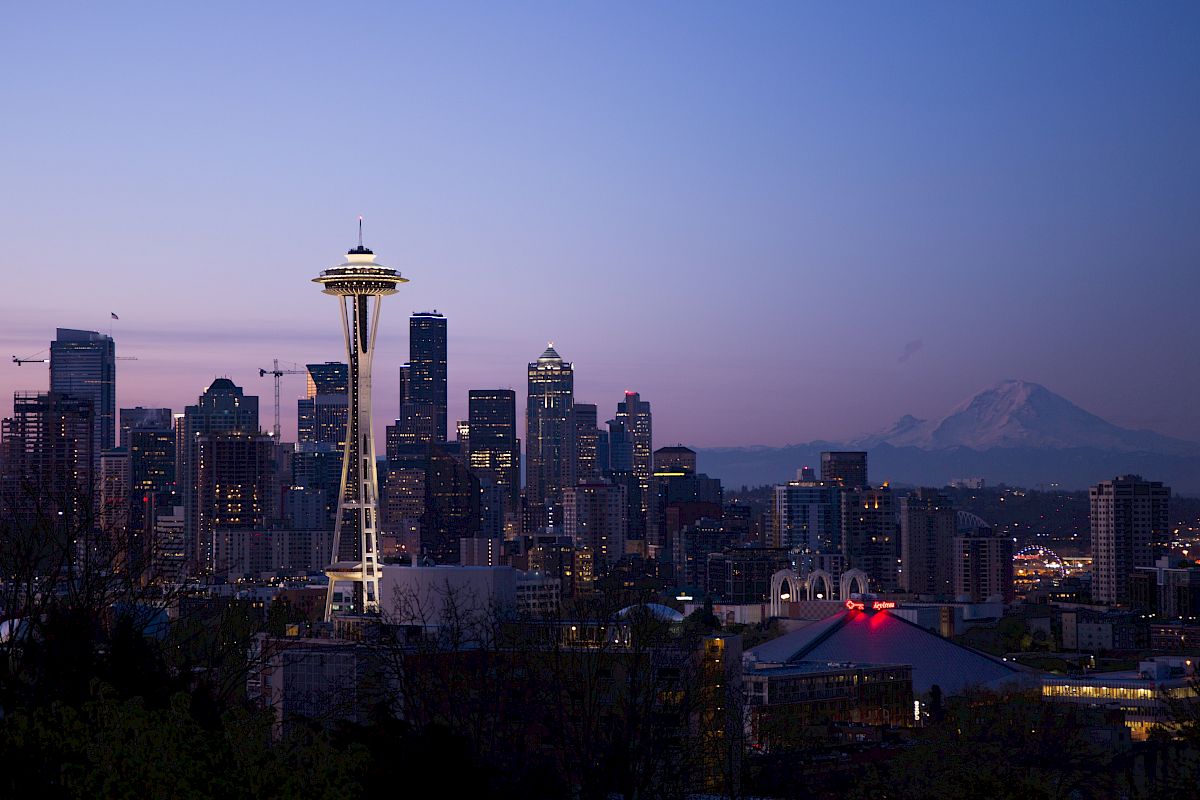 The image shows the Seattle skyline at dusk with the Space Needle prominent and Mount Rainier visible in the background.