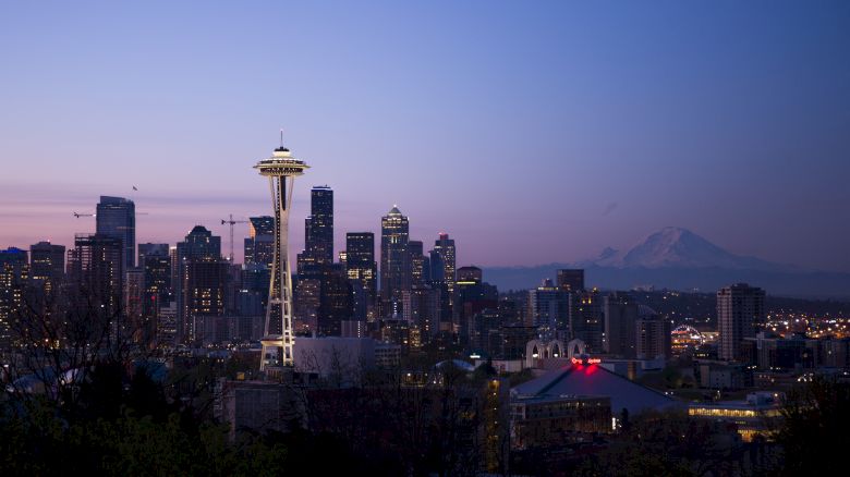 The image shows the Seattle skyline at dusk with the Space Needle prominent and Mount Rainier visible in the background.