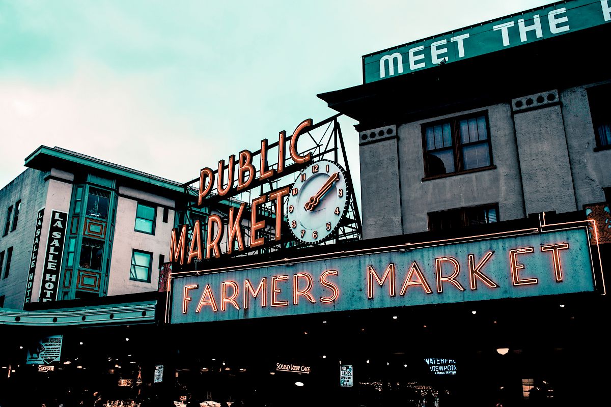This image shows a neon sign advertising a Public Market and Farmers Market, likely taken at a well-known marketplace in an urban area during the day.
