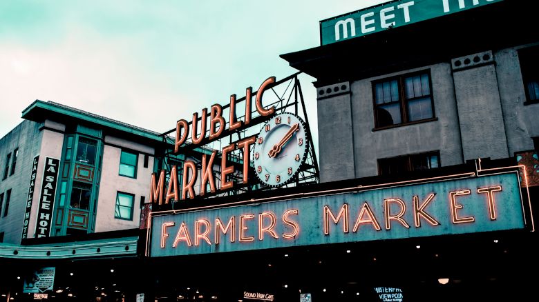 This image shows a neon sign advertising a Public Market and Farmers Market, likely taken at a well-known marketplace in an urban area during the day.